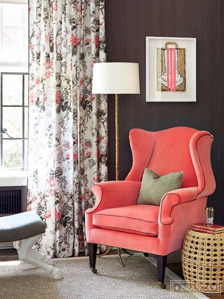 Bright pink coral wing chair in front of floral drapes