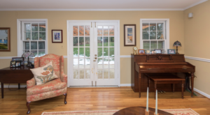 Living room with French doors, gold walls, chair rail, upright piano and pink toile wingback chair