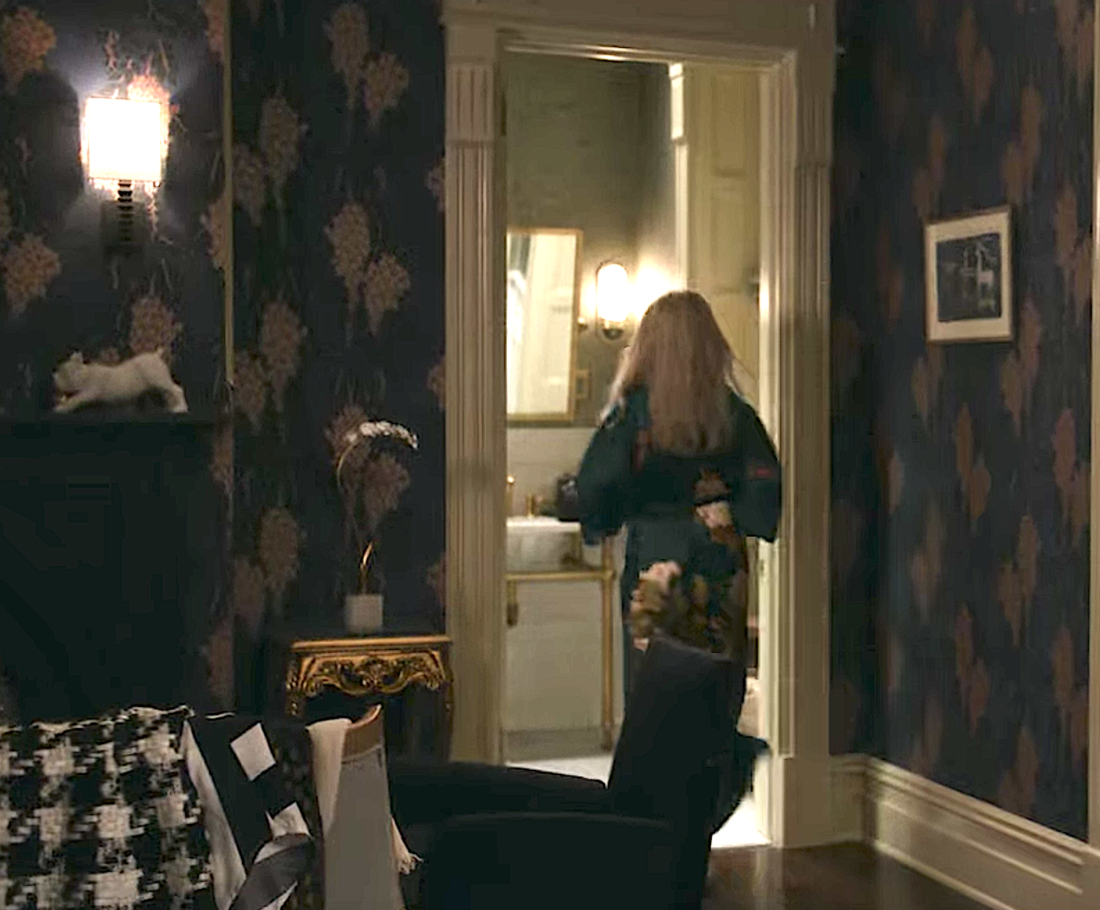 Woman in robe entering bathroom from fancy bedroom