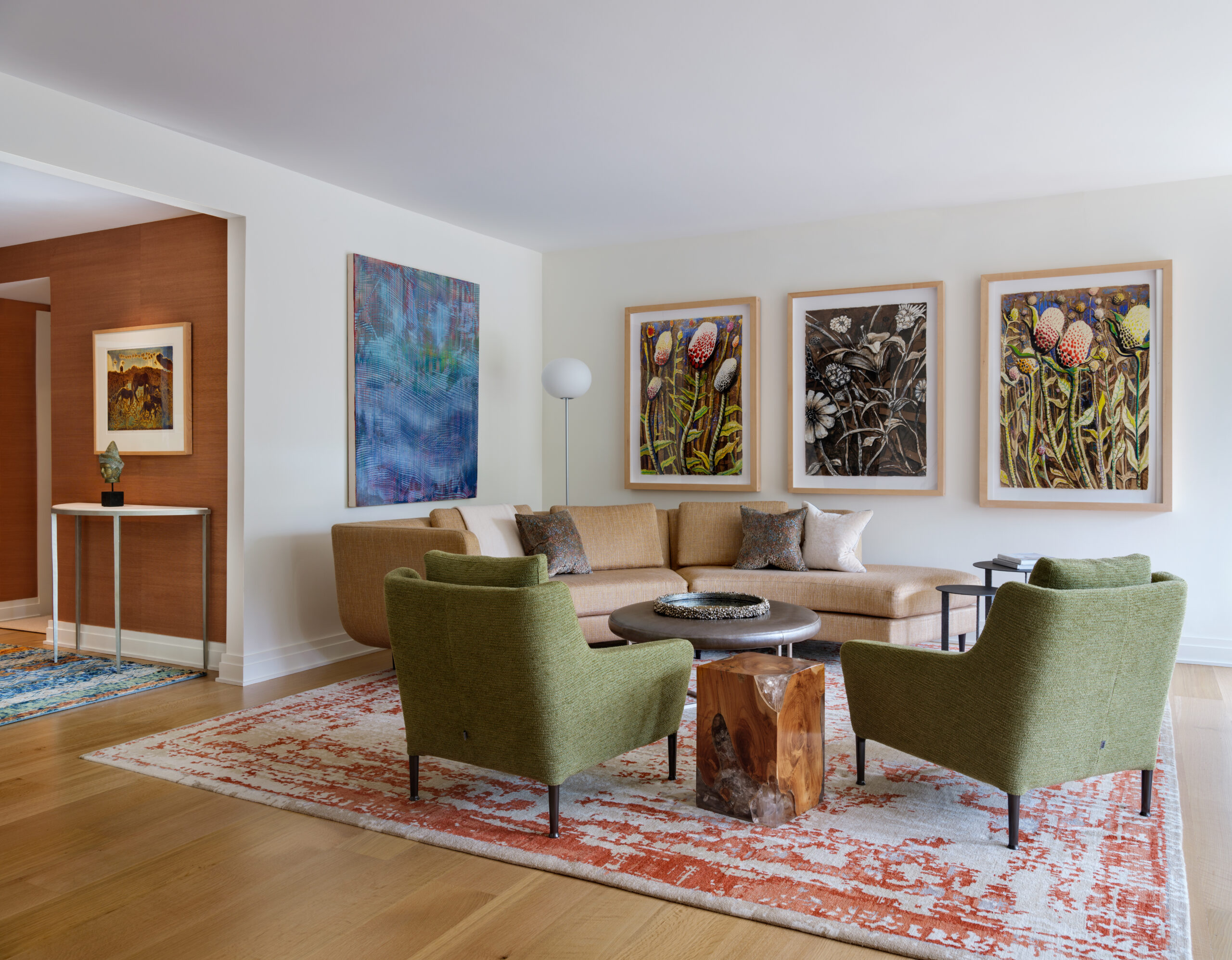 Living room with curved tan sofa, green lounge chairs, side tables, and art.