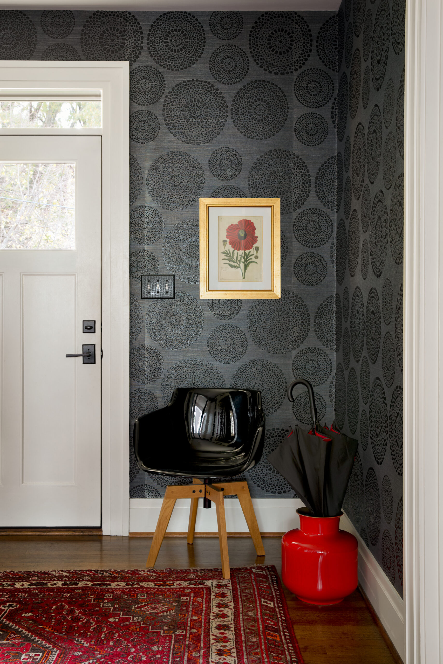 Foyer with black patterned wallpaper, red rug, black chair and red pot.