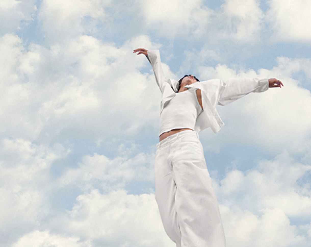 Person in white jumping against a blue sky with clouds
