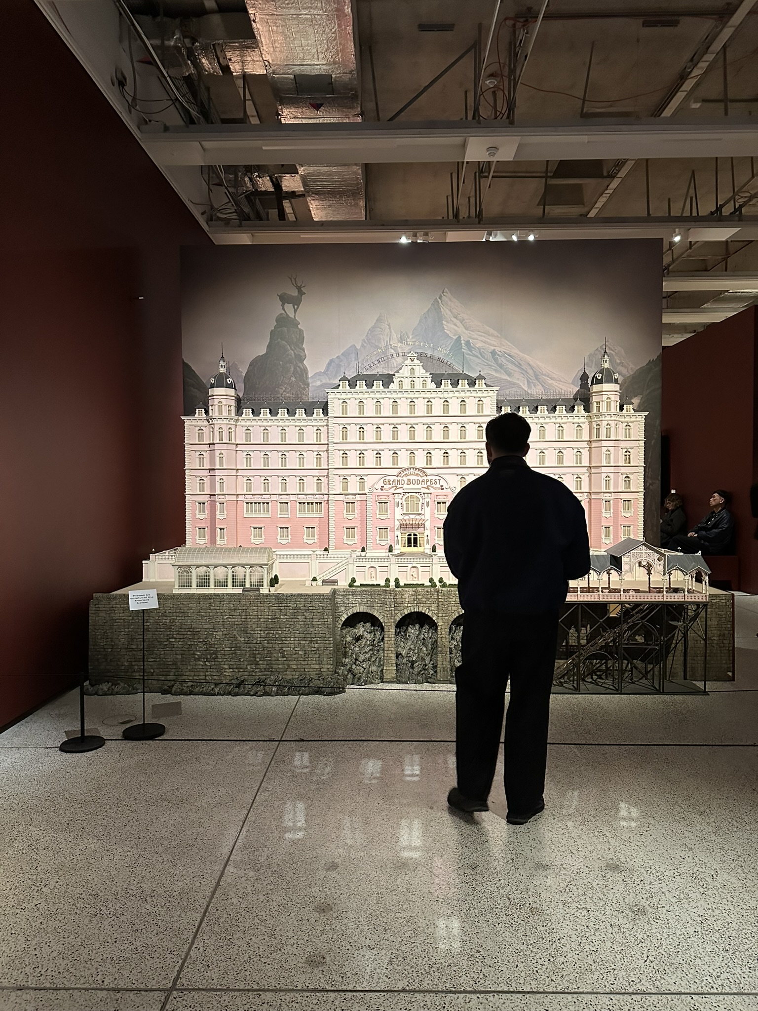 Man standing in front of a large-scale model of a grand, symmetrical pink building