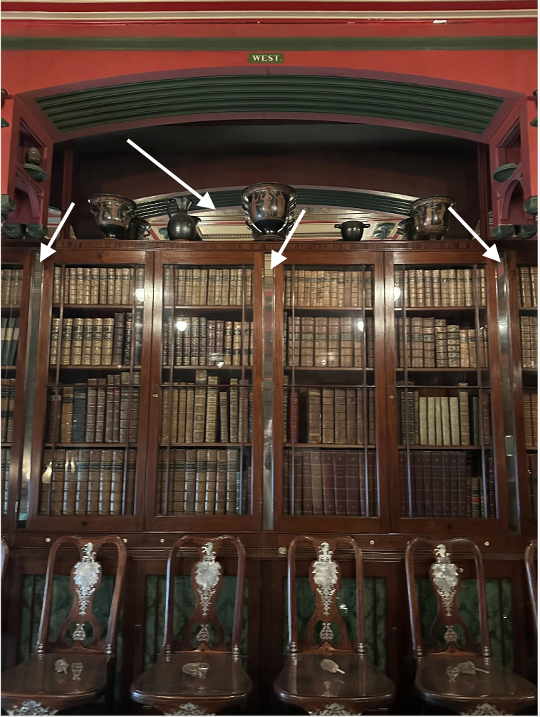 Historic library with vertical mirrors between bookcases and behind arch above and arrows pointing them out.