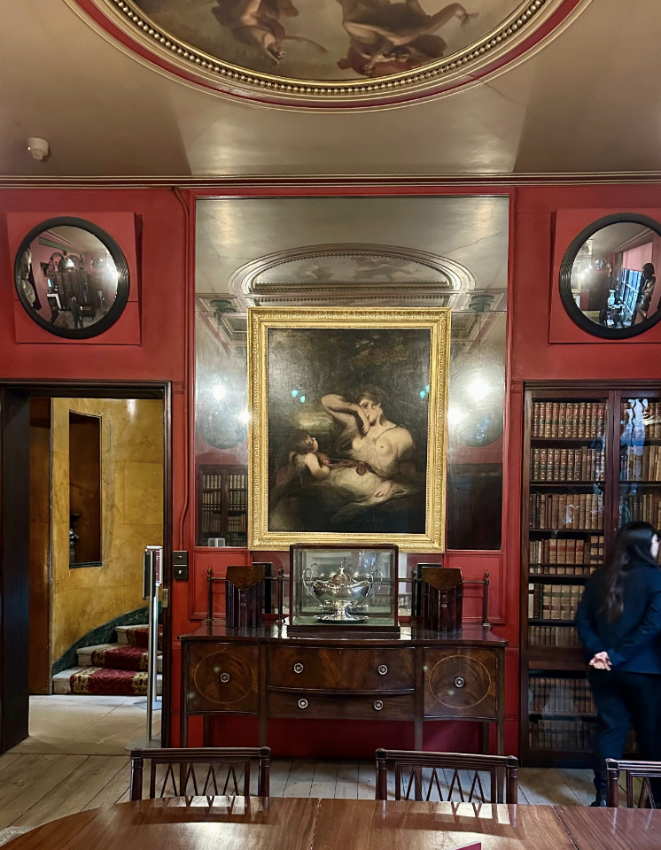 Red room with two convex mirrors and a painting hung on a mirror over a piece of furniture