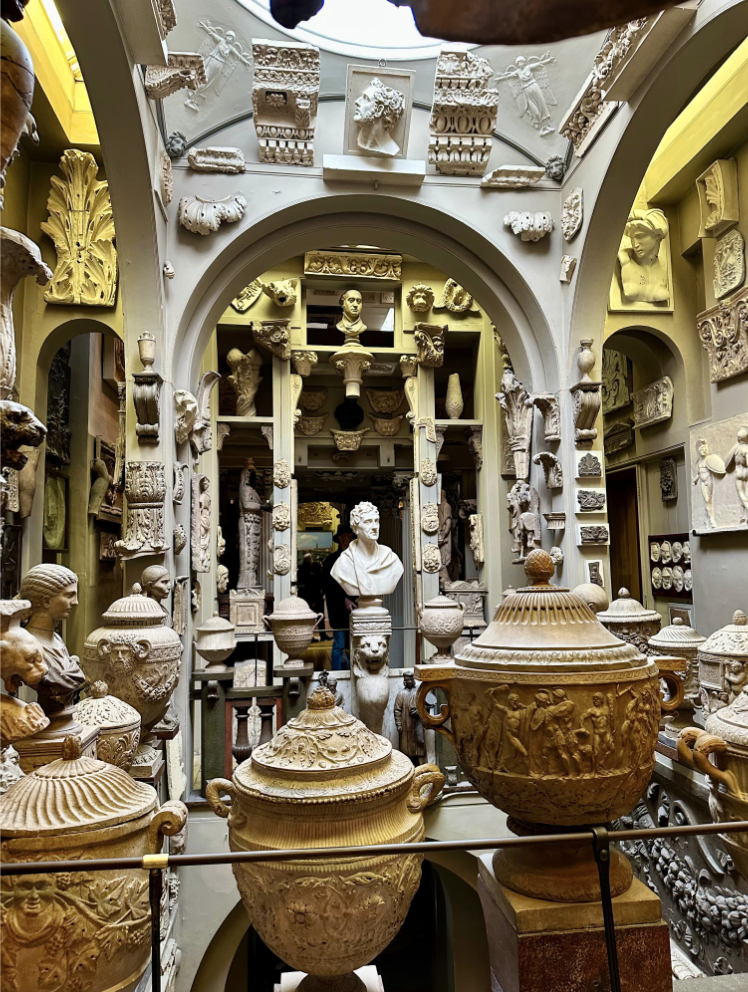 Museum room crowded with antiquities, statues, architectural elements.
