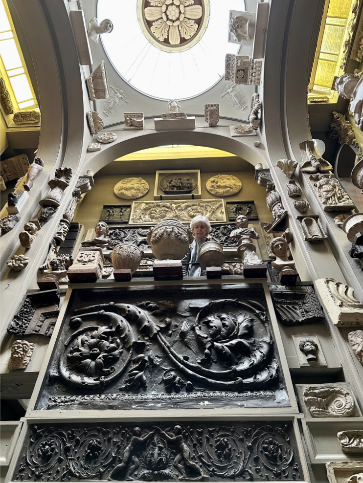 Museum room with domed skylight crowded with antiquities, statues, architectural elements.