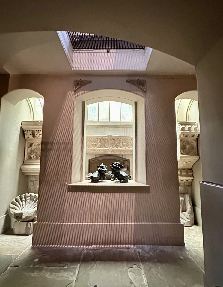 Basement-level museum room with antiquities and hole in ceiling with grille.