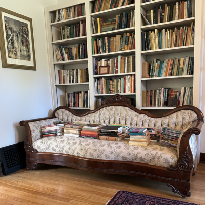 Victorian sofa with stacks of books in front of a bookcase