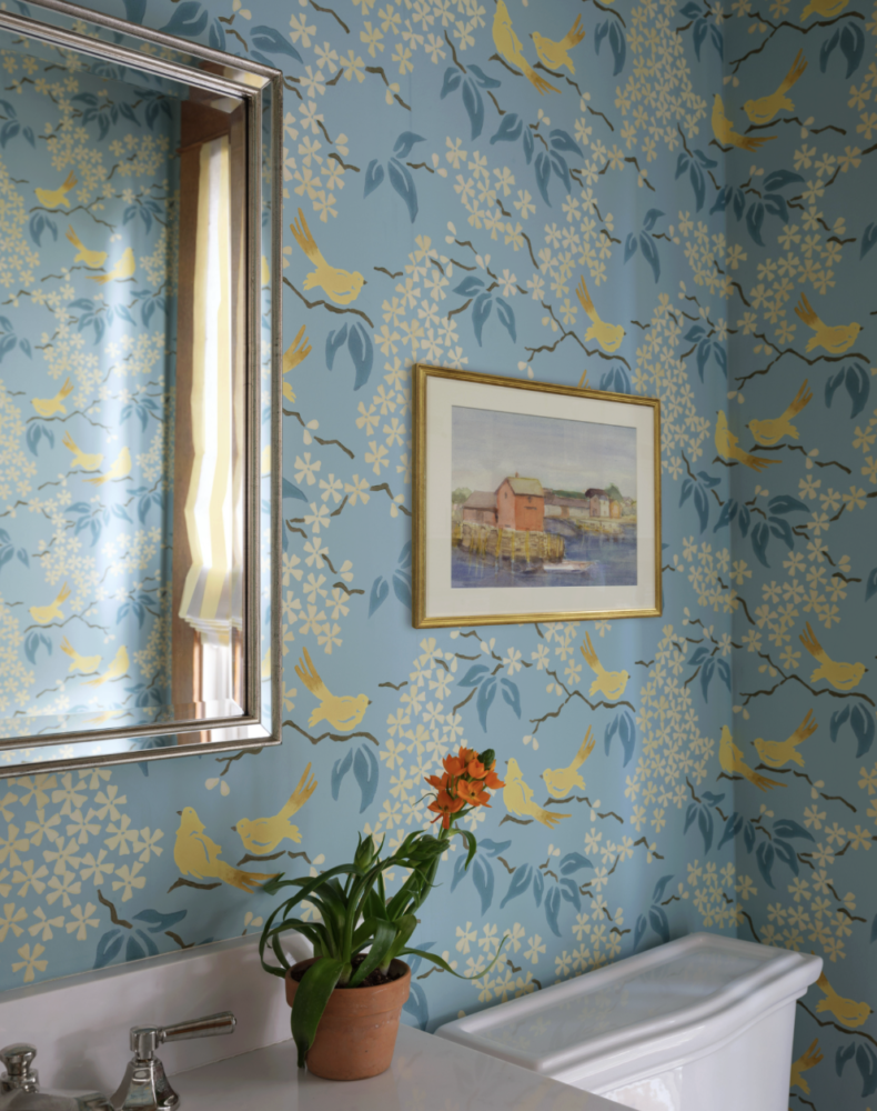Painting of seaside hanging on bird printed wallpaper.