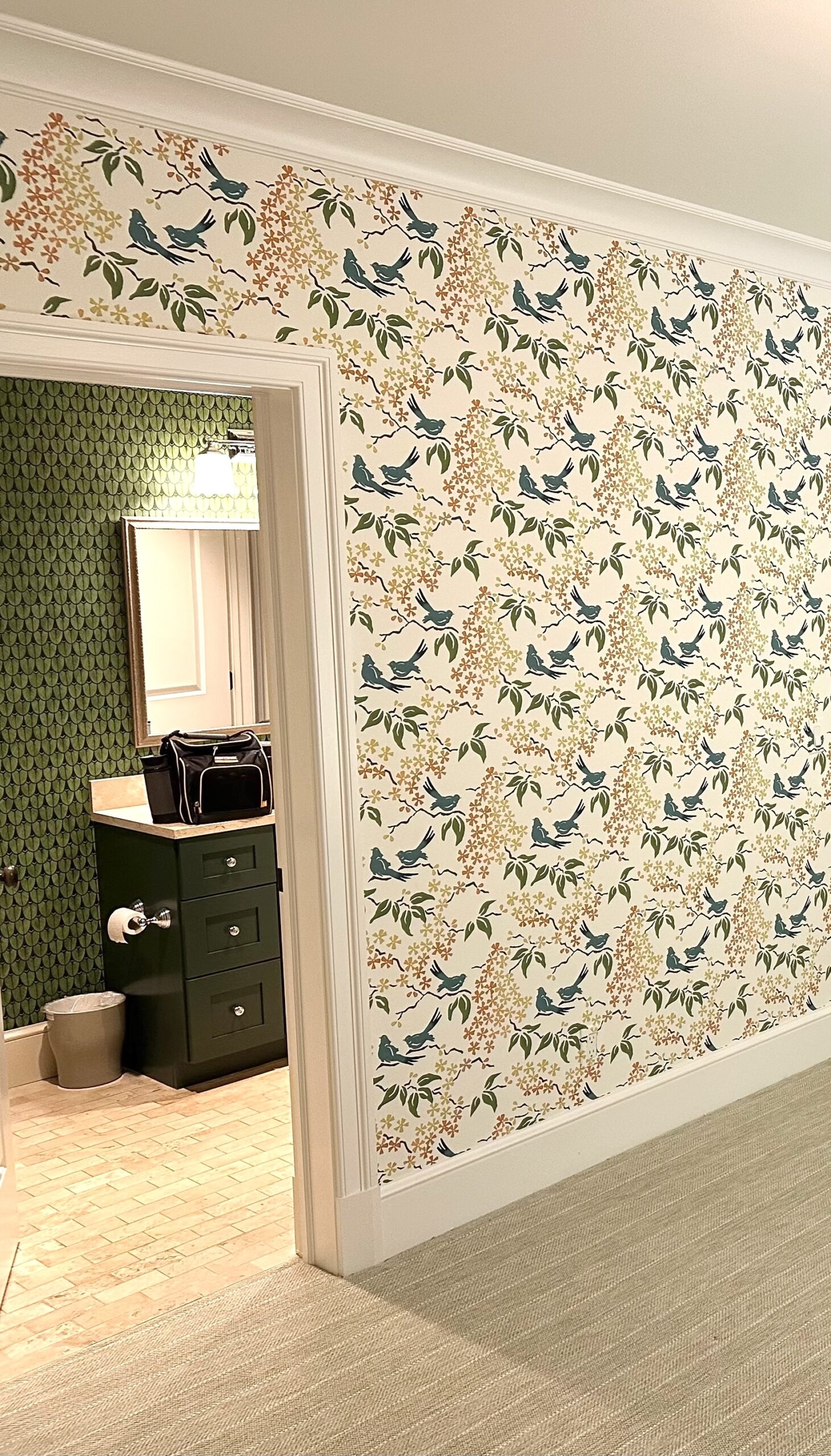 Bird wallpaper on walls outside of bathroom with geometric, green wallpaper.