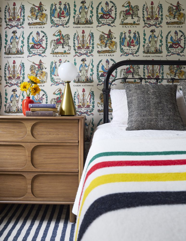 Bedroom with wallpaper, striped rug, and striped blanket