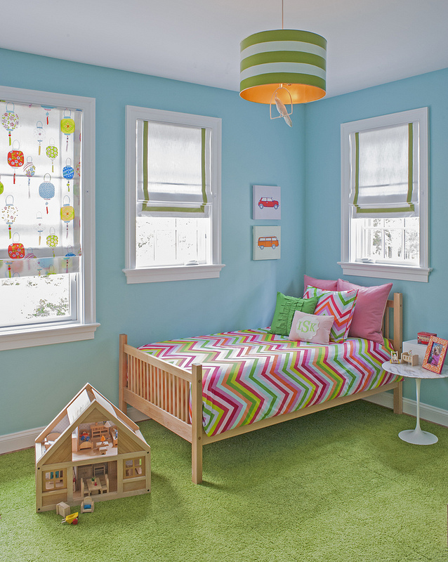 Light blue child's bedroom with colorful bedspread and green rug